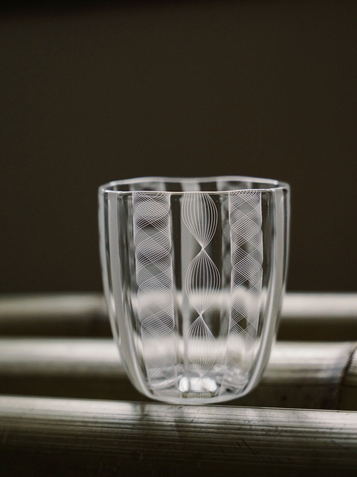 Clear glass tumbler cut with fine vertical lines that catch the light like lacework.