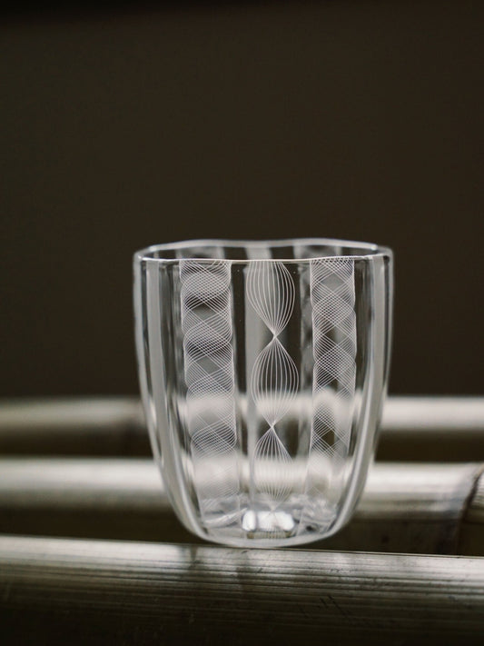 Clear glass tumbler cut with fine vertical lines that catch the light like lacework.