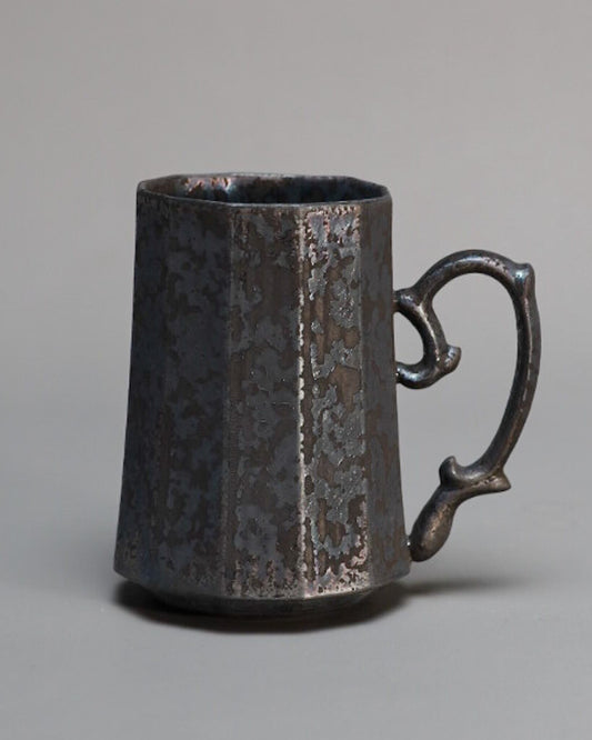 Tall faceted mug in dark metallic glaze with a scrolled handle and a finely pitted surface.