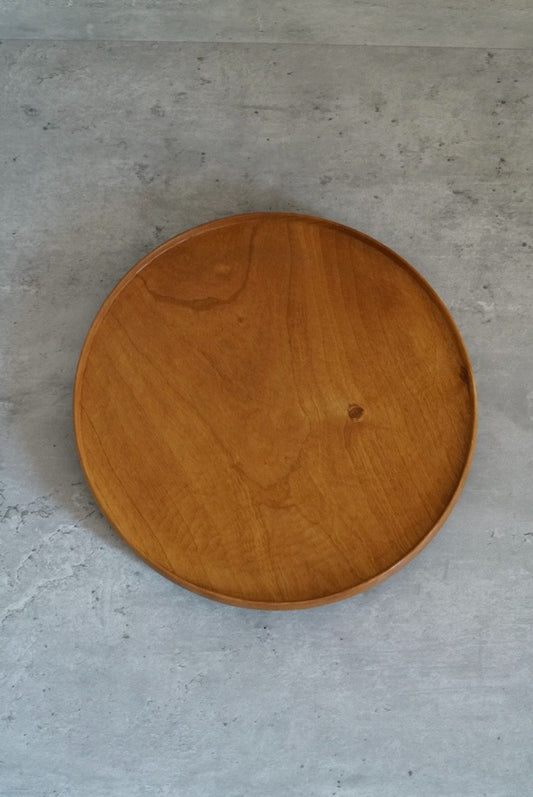 Round wooden tray in warm honey brown cherry wood, its grain sweeping across the face.