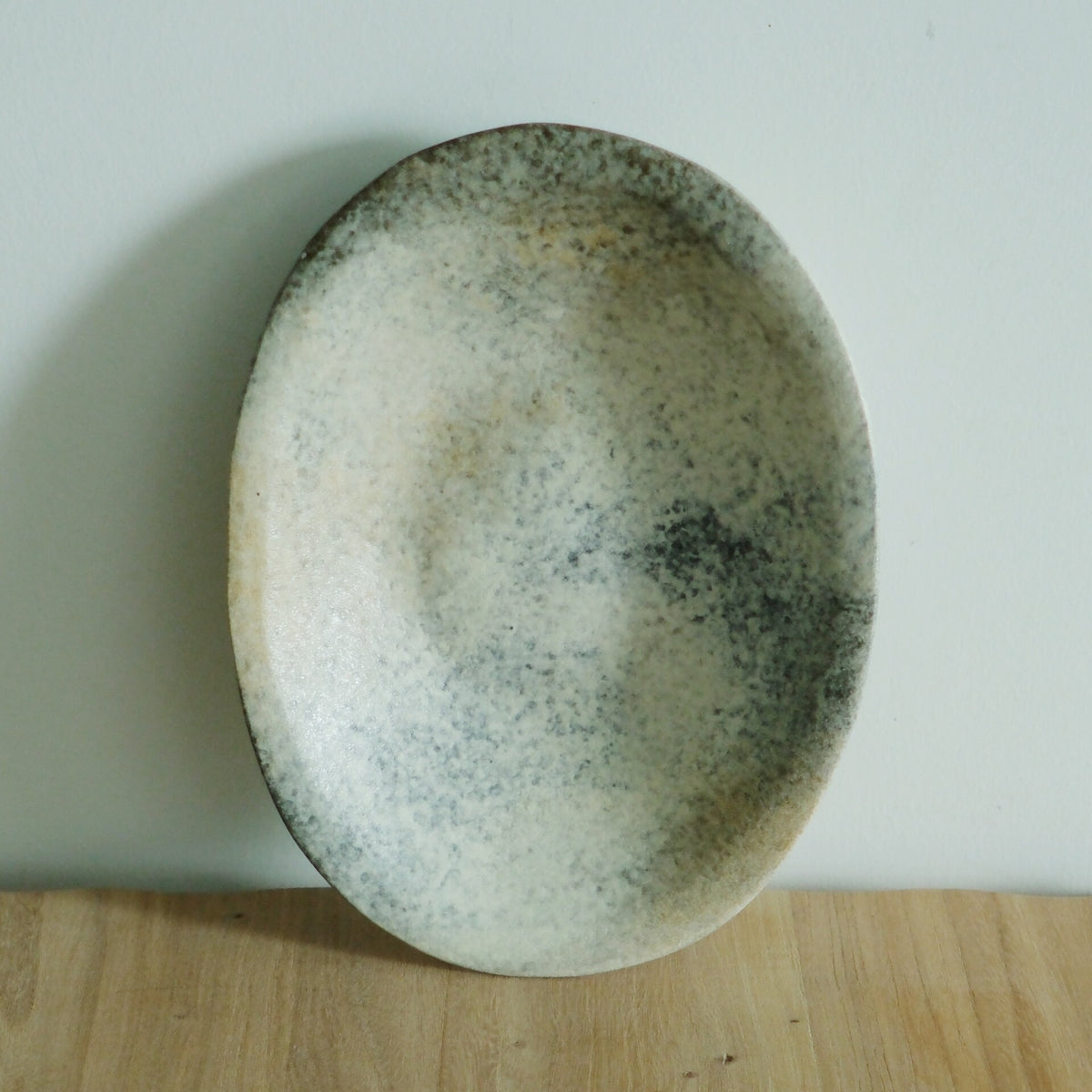 Oval plate in soft sea green speckled with darker flecks, standing against a pale wall.