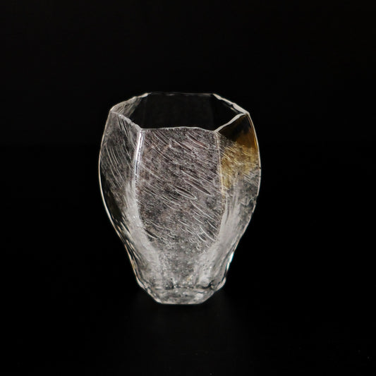 Hexagonal clear glass cup with a frosted crackled surface and a warm amber patch, on black.
