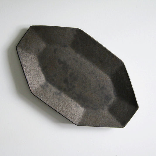 Octagonal plate in matte iron brown, its faceted rim cut in clean angular planes.