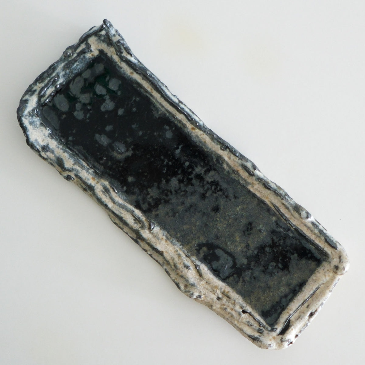 Long rectangular dish with a dark glazed well and rough torn cream edges.