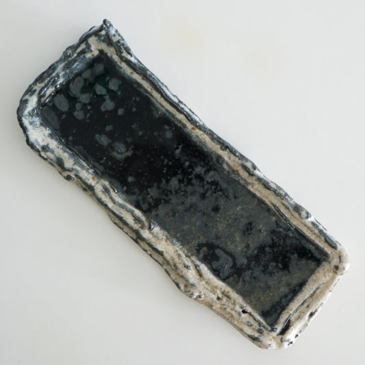 Long rectangular dish with a dark glazed well and rough torn cream edges.