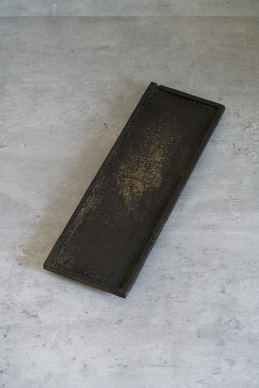 Long narrow tray in dark lacquer with a mottled gold sheen breaking across its surface.