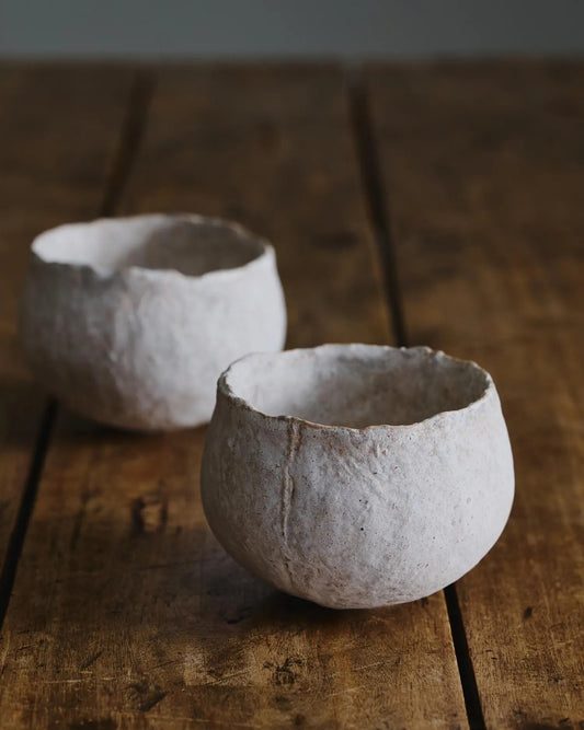 Two rough white cups with torn, uneven rims and a chalky incised surface, on weathered floorboards.