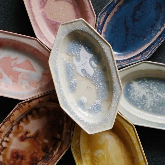 An octagonal white plate with bubbling glaze, laid over a fan of pink, blue and amber plates.