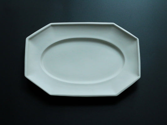 Octagonal celadon plate in soft blue-green with a wide flat rim, lit against black.