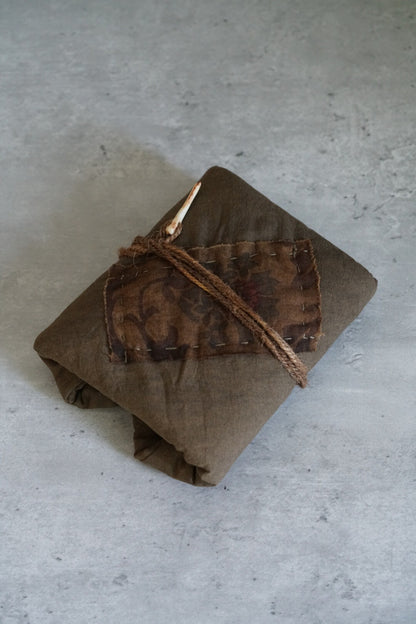 Folded persimmon-dyed cloth mat in warm russet, tied with a slim leather cord.