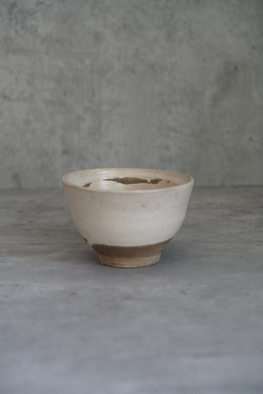Footed bowl in chalky cream slip with a dark patch at the rim and a bare clay foot.