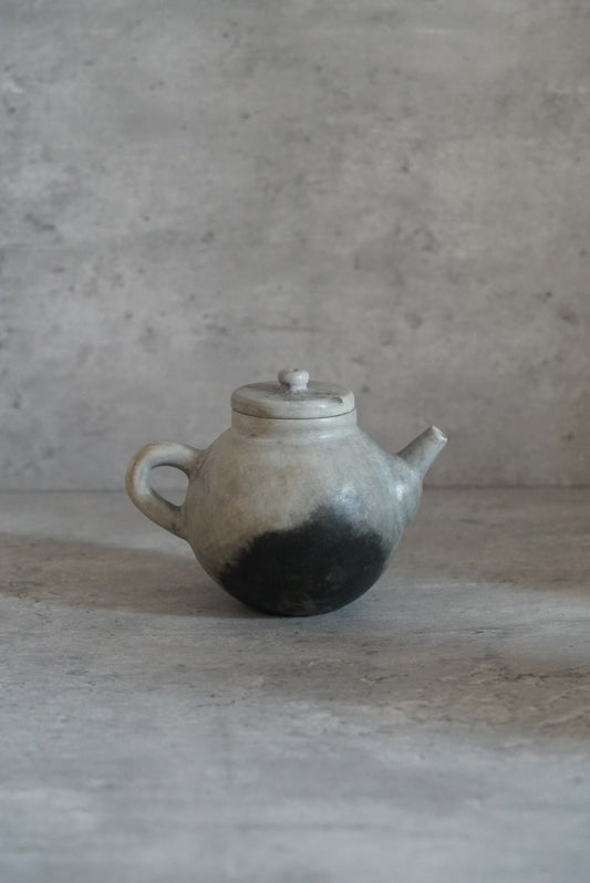 Small round teapot with a loop handle, speckled grey above a scorched black base.