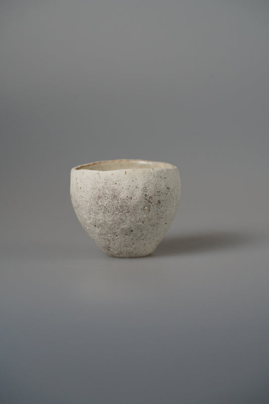 Small cream cup with a rough grainy surface and a rust-marked rim, on pale grey.