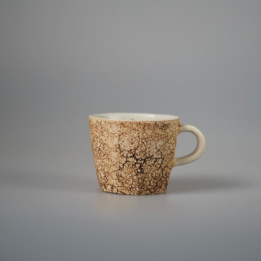 Cream mug with a crackled speckled glaze and a small loop handle, on pale grey.