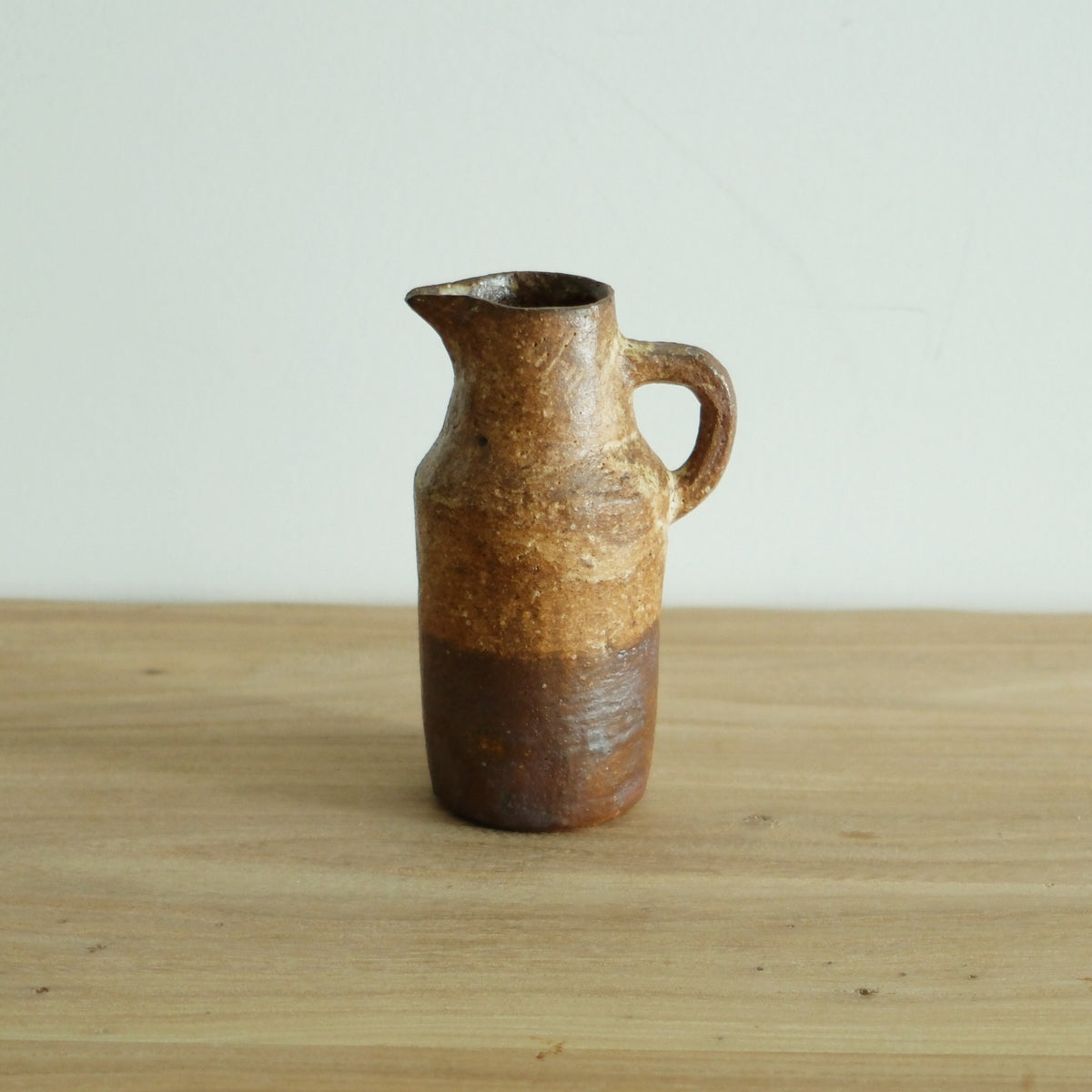 Small wood-fired jug with a slim neck and loop handle, sandy orange above a darker foot.