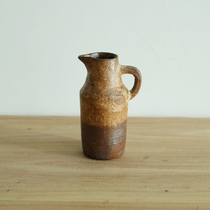 Small wood-fired jug with a slim neck and loop handle, sandy orange above a darker foot.