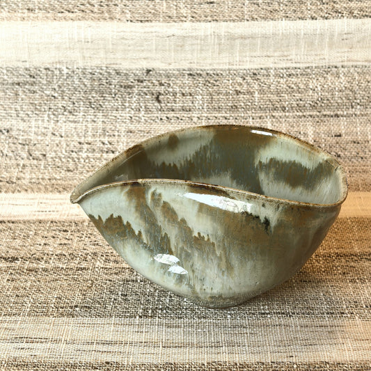 Pouring bowl with a pinched spout, its cream and green glaze running in soft streaks, on woven matting.