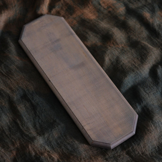 Long narrow wooden board with clipped corners and a smooth dark finish, on brown cloth.