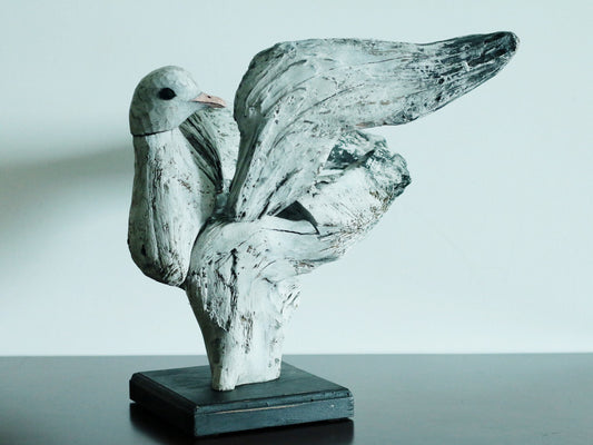 Carved wooden seagull with outstretched wings, finished in weathered white and grey, on a black base.