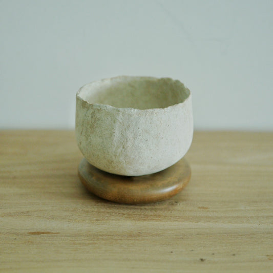 Deep cream cup with a coarse chalky surface, standing on a small round wooden stand.