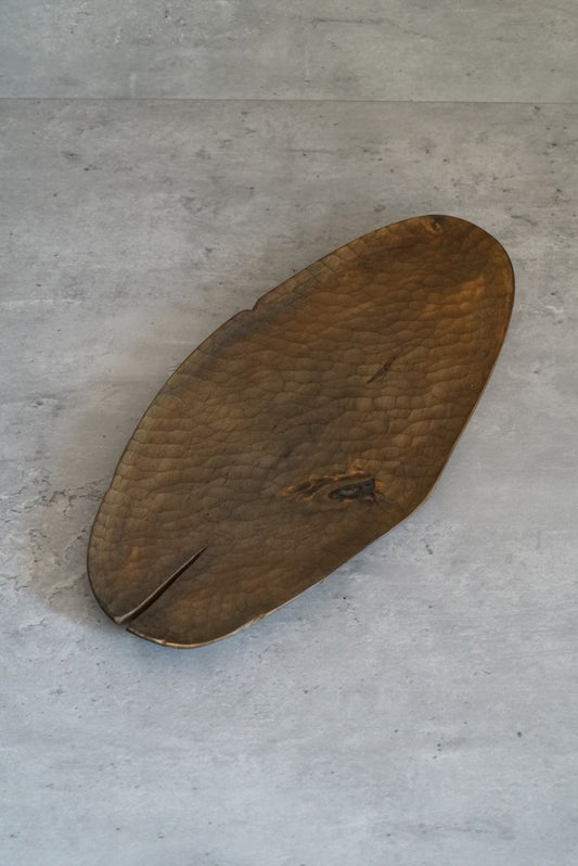 Long oval wooden tray with a rippled carved surface and a natural split at one end.