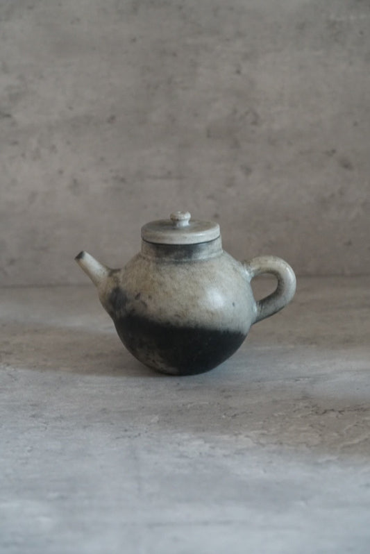 Small round teapot with a side handle, mottled grey above a deep black scorched base.