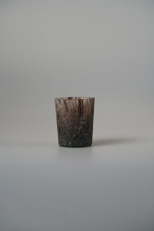 Small glass cup in mottled brown with a bark-like textured surface, on pale grey.