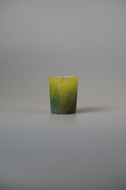 Small glass cup graded from yellow to deep green with a mottled speckled surface.