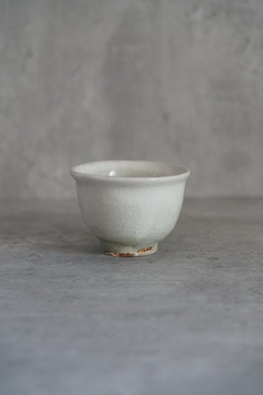 Small footed cream cup with a flared rim and a rust-marked foot, on grey concrete.