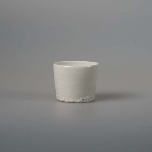 Small plain white porcelain tea cup with straight sides, on a pale grey ground.