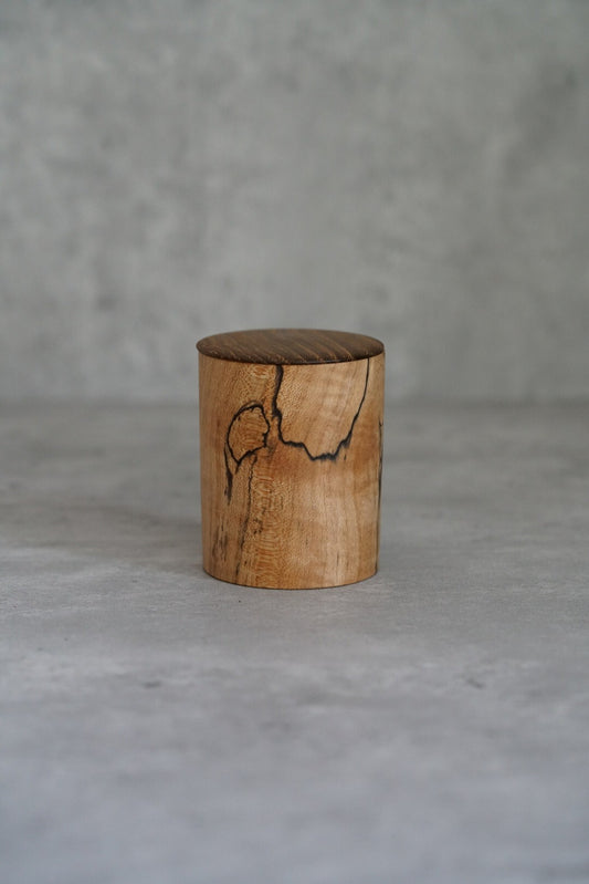 Small lidded wooden jar turned from pale maple, with a dark natural crack across the lid.