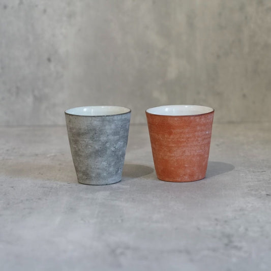 Two small cups side by side, one mottled grey-blue and one warm terracotta orange.