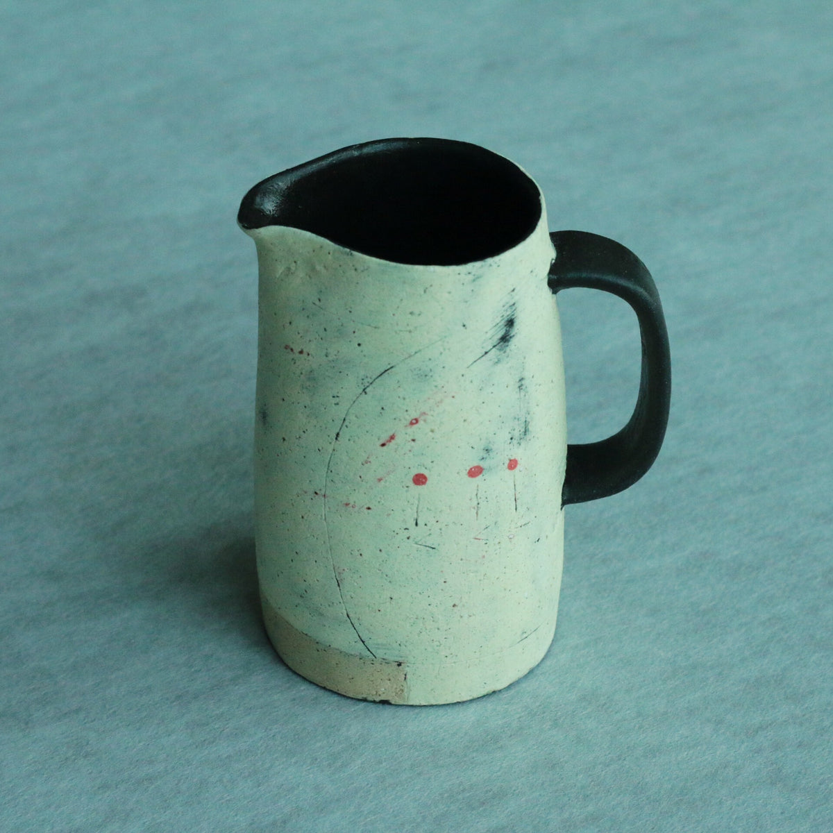 Speckled pale green pitcher with a black rim and handle, flecked with tiny red and blue marks.