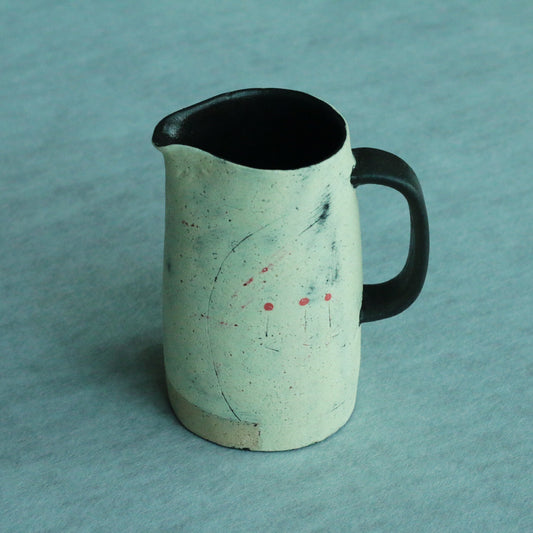 Speckled pale green pitcher with a black rim and handle, flecked with tiny red and blue marks.