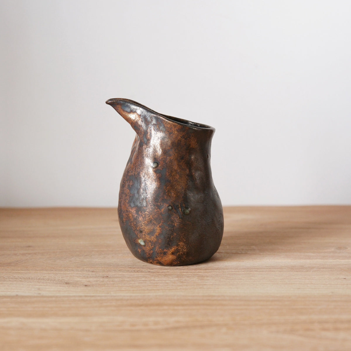 Bronze-glazed pouring jug with a full belly and a long drawn lip, on a wooden table.
