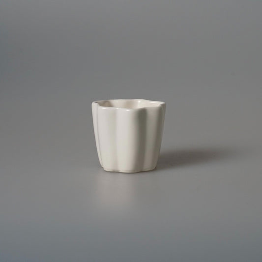 Small white porcelain cup with softly faceted sides, on a pale grey ground.
