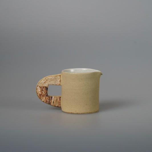 Small cream pouring vessel with a drawn lip and a rough, pierced clay handle.
