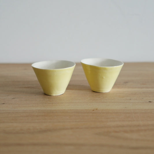 Two small pale yellow porcelain tea cups with flared rims, side by side on a wooden table.