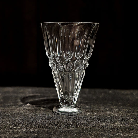 Small footed glass cup flaring sharply outward, cut with vertical ribs and a row of beads.