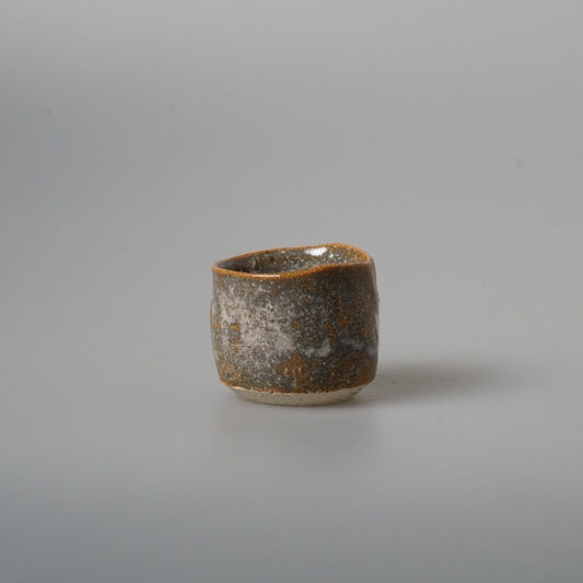 Tiny wood-fired cup in mottled brown and grey with a rough scorched surface.