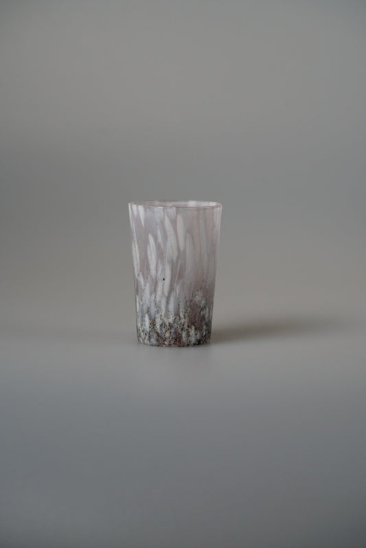 Tall glass cup in mottled white and soft pink with a finely flecked surface.