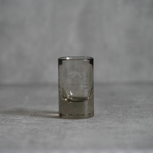 Small smoky grey glass sake cup with a heavy base and softly dented sides.