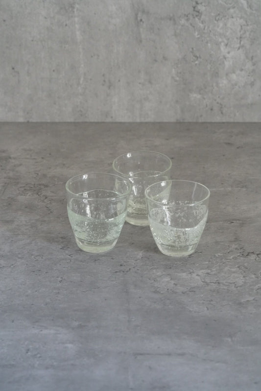Three small pale green glass cups standing together on a rough grey concrete surface.