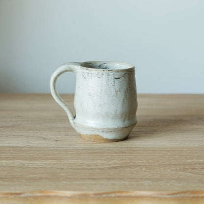 Tall pale grey-white mug with a rough crawled glaze and a large curved handle.