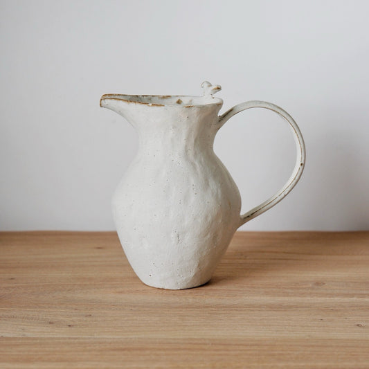 White jug with a rough dimpled surface, a drawn lip and a slim looping handle.