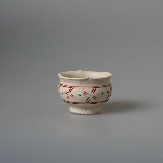 Small footed cream cup painted with a band of fine red dashes and green marks.