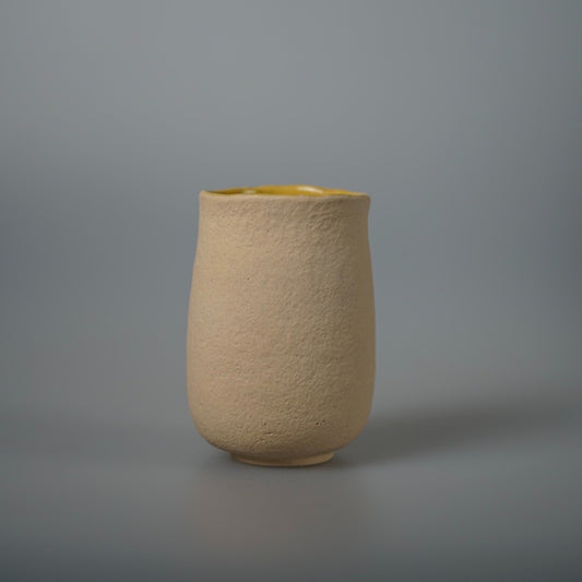 Tall cream ceramic tumbler with a coarse unglazed outer surface and a smooth pale yellow glaze inside the rim.