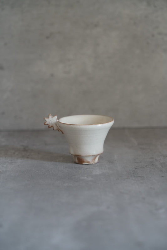 Small white footed cup with a jagged crown-like spur rising from one side of the rim.