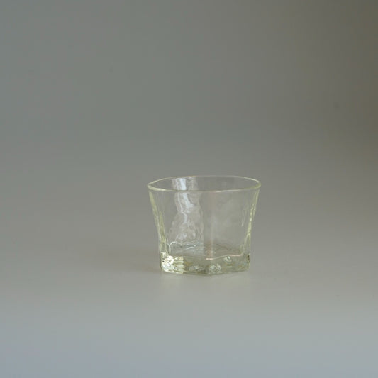 Small hexagonal glass cup with cut faces and a pale yellow-green tint, on a pale ground.