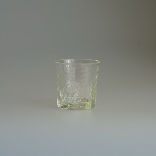 Hexagonal glass cup with faceted sides and a faint yellow-green cast, on a pale ground.